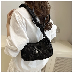 Detalle del bolso negro con textura floral, colgante de corazón plateado y lazo