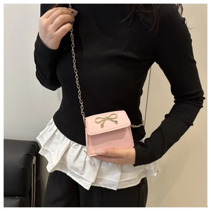 Detail of pink saddle bag with golden bow hardware and delicate metal chain strap