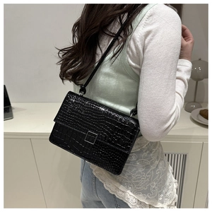 Detail of black crocodile texture bag with silver buckle worn over shoulder on a model