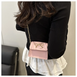 Close-up of pink mini saddle bag with golden bow and chain strap on shoulder