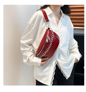 Detail of red patent leather waist bag with silver chain and wide fabric strap
