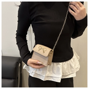 Detail of a beige mini flap crossbody bag with a gold bow metal buckle and chain strap