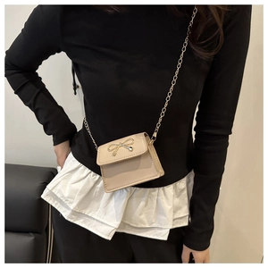 Detail of beige saddle bag featuring gold bow buckle and chain strap on a model