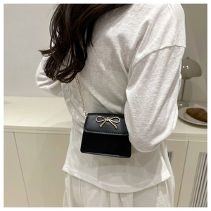 Chic black saddle bag with golden bow hardware and chain strap shown in a lifestyle setting