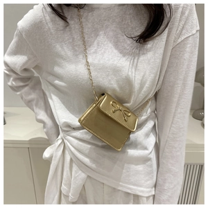 Detail of a golden mini crossbody bag with a 3D bow and elegant chain shoulder strap