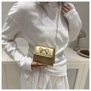 Close-up of golden mini crossbody bag with metal bow buckle on a model's outfit