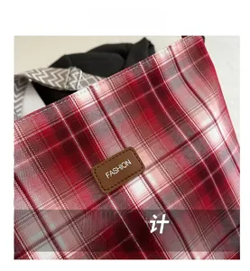 Close-up of red plaid fabric bag featuring a brown leather FASHION label and geometric strap