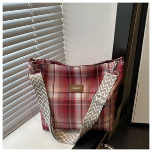 Detail of red plaid tote bag featuring wide geometric strap and metal hardware buckle