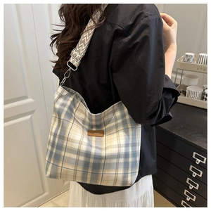 Detail of checkered tote bag with woven shoulder strap and brown leather logo tag