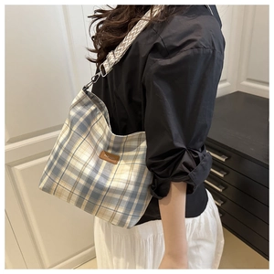 Detail of blue plaid canvas tote bag with brown leather label and geometric shoulder strap