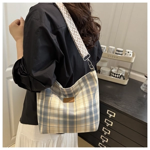 Detail of blue and yellow plaid hobo bag featuring wide geometric strap and logo patch