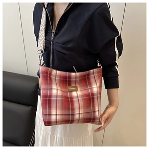 Close-up of red plaid tote bag featuring a woven strap and leather fashion patch
