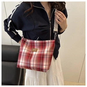 Detail of red plaid canvas tote bag with wide patterned strap and leather fashion label