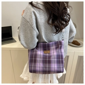 Detail of purple plaid canvas bag featuring leather logo patch and zigzag woven shoulder strap