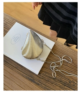 Close-up of a silver shell-shaped metallic crossbody bag with a snake bone chain strap