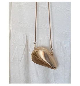 Macro detail of golden shell-shaped metal clutch with vertical texture and snake chain