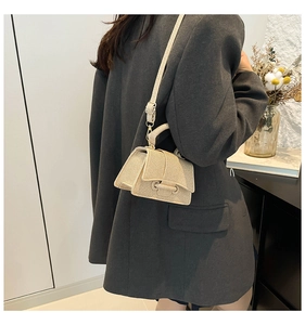 Close-up of beige textured mini square bag with unique circular clasp on a black blazer