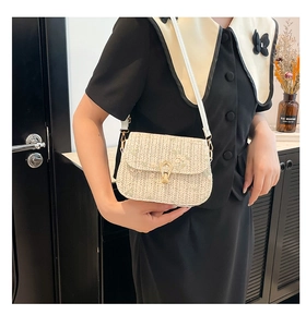 Close-up of beige woven saddle bag with gold U-shaped buckle and white leather strap