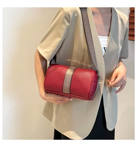 Détail du sac cylindrique rouge en cuir grainé avec sa large bandoulière géométrique