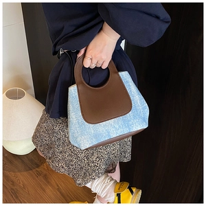 Detail showing blue denim fabric and brown leather handle of the stylish handbag