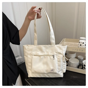 Gros plan sur le sac fourre-tout beige en nylon avec poche avant zippée et étiquette