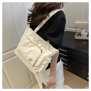 Close-up of white nylon tote bag with zipper pocket and good luck patch detail