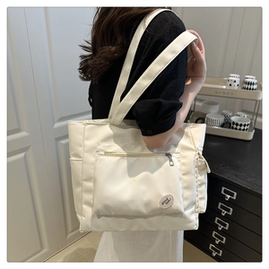 Close-up of the beige canvas tote bag showing the front zipper pocket and side pockets