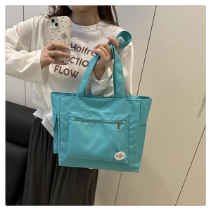 Close-up of light blue nylon tote bag with zipper pocket and good luck patch detail