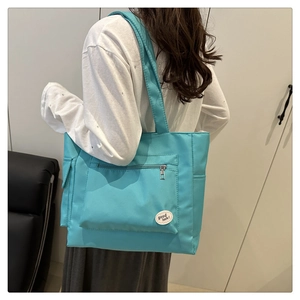 Detail of light blue nylon tote bag with front zipper pocket and good luck label