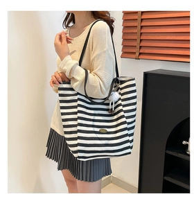Dettaglio borsa tote in tela a righe bianche e nere con tracolla in pelle e ciondolo fluffy