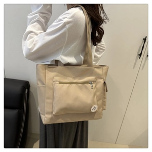 Detail of khaki tote bag with front zipper pocket and decorative 'good luck' emblem