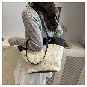 Detailed back view of a large woven straw and black leather patchwork tote bag on a model
