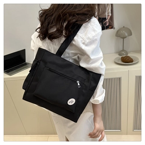 Close-up of black canvas tote bag showing the zipper front pocket and good luck patch