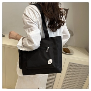 Détail du cabas en nylon noir avec poche zippée avant et étiquette décorative porte-bonheur
