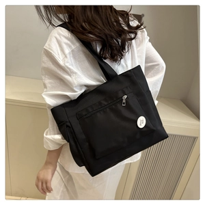Gros plan du sac cabas en toile noire avec poche zippée externe et écusson Good Luck