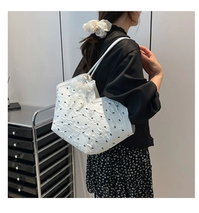 Detailed view of white quilted tote bag featuring black bow prints and lace pearl charm