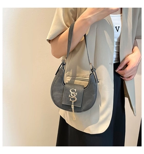 Primer plano de bolso media luna gris con logotipo dorado y borlas de metal