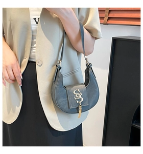 Detalle de bolso medialuna gris con logo SS dorado y borla colgado del hombro