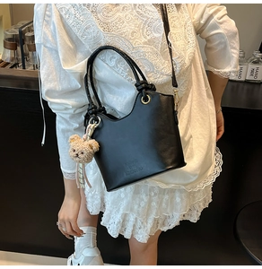 Secchiello chic in pelle nera indossato da una modella con ciondolo a orso e manico in metallo