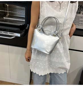 Borsa a secchiello metallizzata argento con manico e logo in rilievo in un contesto casual
