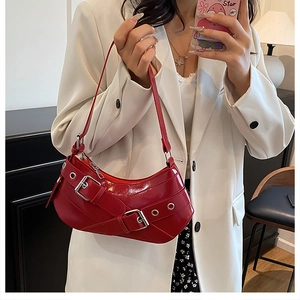Close-up of red patent leather shoulder bag with silver metal eyelets and belt buckle
