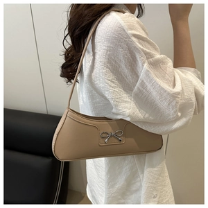 Detail of elegant beige underarm bag with silver bow ornament worn by a model