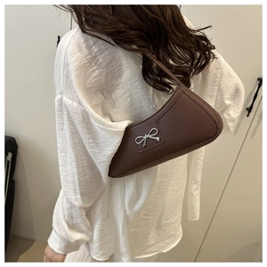 Detail of a brown leather shoulder bag with a silver bow ornament on a white shirt