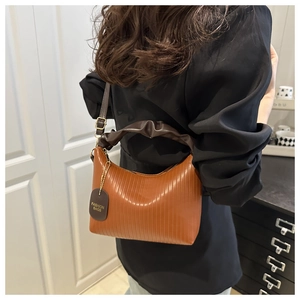 Detail of caramel orange pleated shoulder bag featuring dark brown handle and leather tag