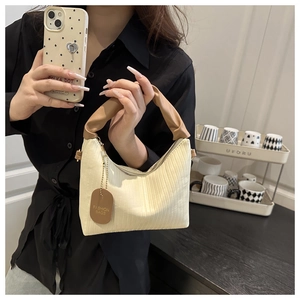 Detail of creamy white pleated handbag with brown leather handle and fashion tag