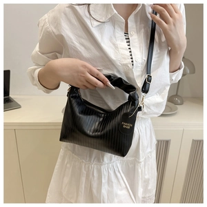 Detail of black pleated shoulder bag with vertical texture and metal strap hardware