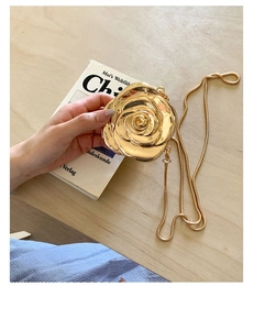 Close-up of golden rose-shaped metal evening clutch with fine snake chain on wooden table