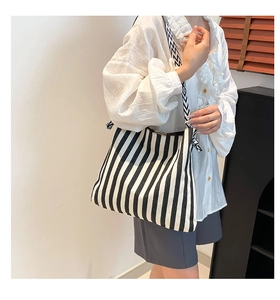Detail of striped canvas tote bag with geometric shoulder strap shown on model in modern setting