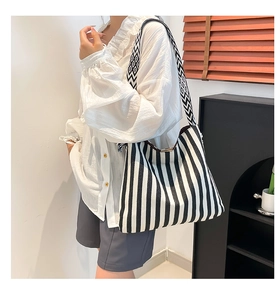 Detailed view of striped canvas tote bag with woven shoulder strap shown on model