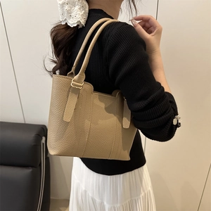 Sac fourre-tout en cuir beige avec garniture dorée porté par un mannequin en intérieur